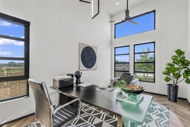 home office featuring a high ceiling, ceiling fan, and light hardwood / wood-style floors