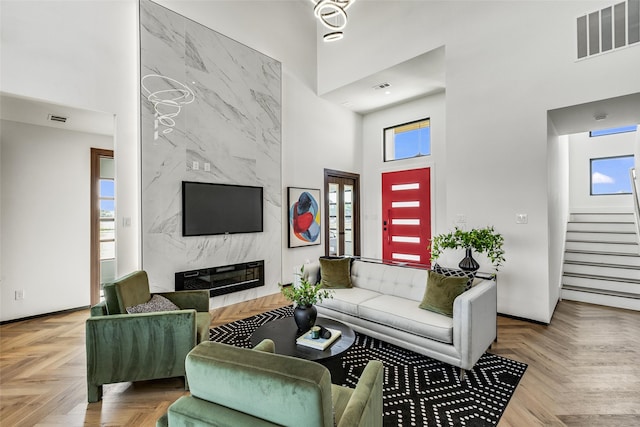 living room with a towering ceiling, a high end fireplace, and light parquet floors