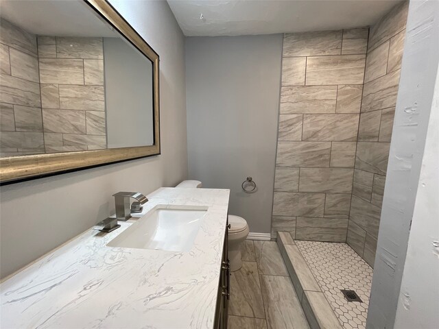 bathroom featuring a tile shower, vanity, and toilet