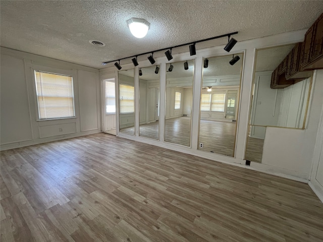 spare room featuring a textured ceiling, light hardwood / wood-style flooring, and rail lighting