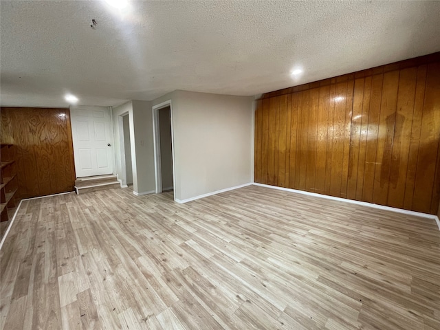 interior space featuring light hardwood / wood-style flooring, wood walls, and a textured ceiling