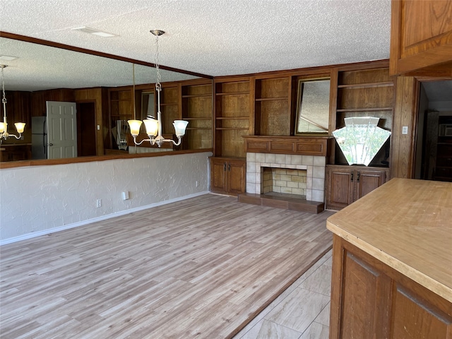 kitchen with a textured ceiling, light wood-type flooring, hanging light fixtures, and stainless steel fridge