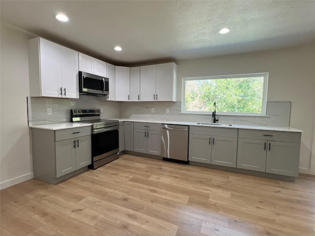 kitchen with gray cabinets, sink, stainless steel appliances, and light wood-type flooring