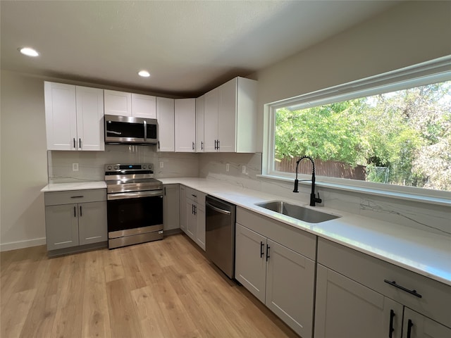 kitchen featuring sink, gray cabinetry, light hardwood / wood-style flooring, appliances with stainless steel finishes, and decorative backsplash