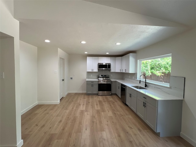 kitchen with sink, light hardwood / wood-style flooring, appliances with stainless steel finishes, gray cabinetry, and decorative backsplash