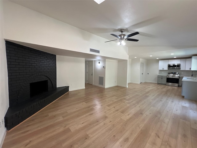 unfurnished living room featuring ceiling fan, sink, a brick fireplace, and light hardwood / wood-style flooring