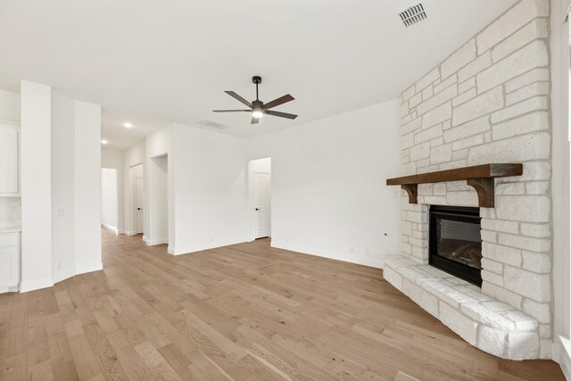 unfurnished living room featuring light hardwood / wood-style flooring, ceiling fan, and a stone fireplace