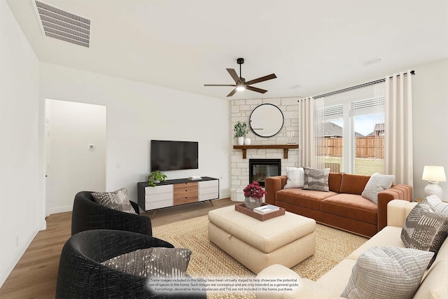 living room with hardwood / wood-style flooring, a stone fireplace, and ceiling fan