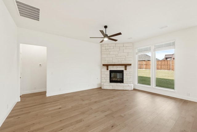 unfurnished living room with light wood-type flooring, a stone fireplace, and ceiling fan