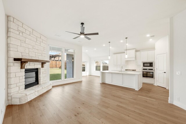 unfurnished living room featuring a fireplace, ceiling fan, light hardwood / wood-style flooring, and sink