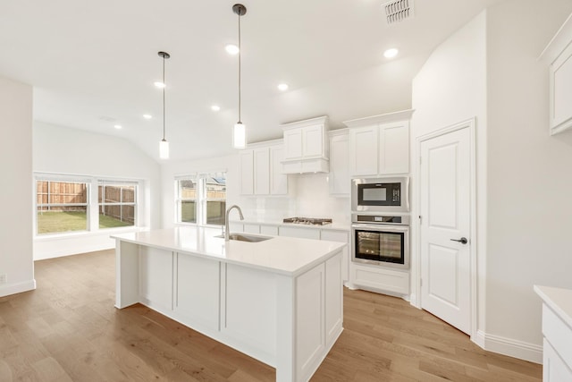 kitchen with appliances with stainless steel finishes, sink, a center island with sink, white cabinets, and hanging light fixtures