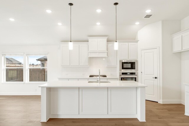 kitchen with light hardwood / wood-style flooring, white cabinetry, hanging light fixtures, and a kitchen island with sink