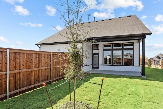 rear view of house with a yard, a patio area, roof with shingles, and fence