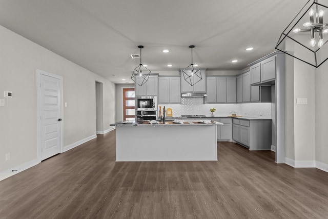 kitchen with dark wood-type flooring, decorative light fixtures, a kitchen island with sink, stainless steel appliances, and gray cabinets