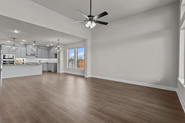 unfurnished living room with recessed lighting, dark wood-style flooring, baseboards, and ceiling fan with notable chandelier