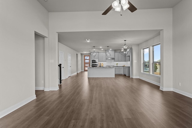 unfurnished living room featuring ceiling fan with notable chandelier, dark wood finished floors, and baseboards