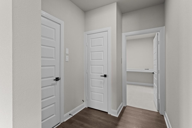 corridor featuring dark wood-type flooring and baseboards