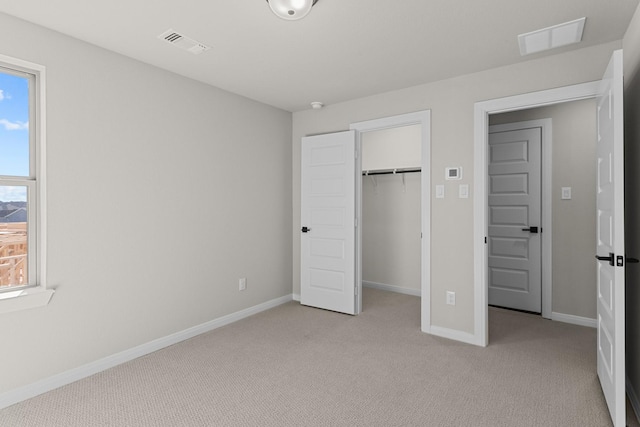 unfurnished bedroom featuring baseboards, a spacious closet, visible vents, and light colored carpet