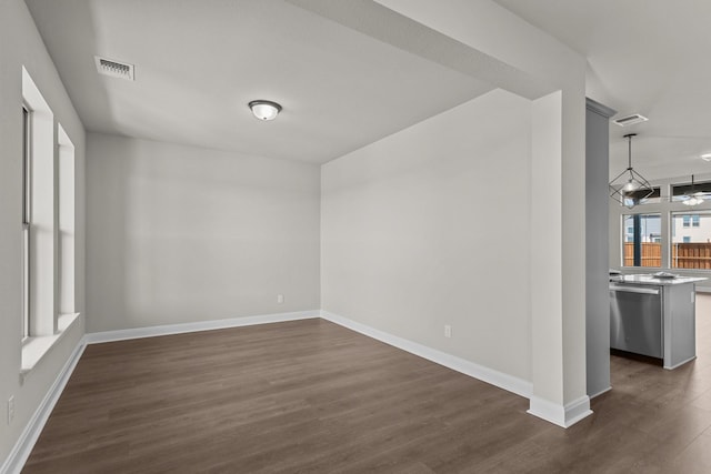 empty room with dark wood-style floors, visible vents, and baseboards