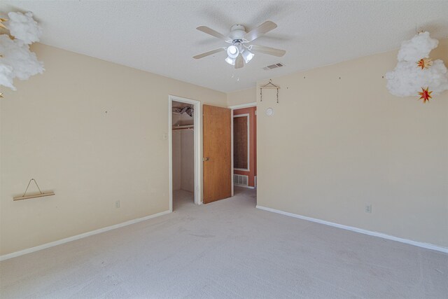 unfurnished bedroom with ceiling fan, a textured ceiling, a walk in closet, light carpet, and a closet