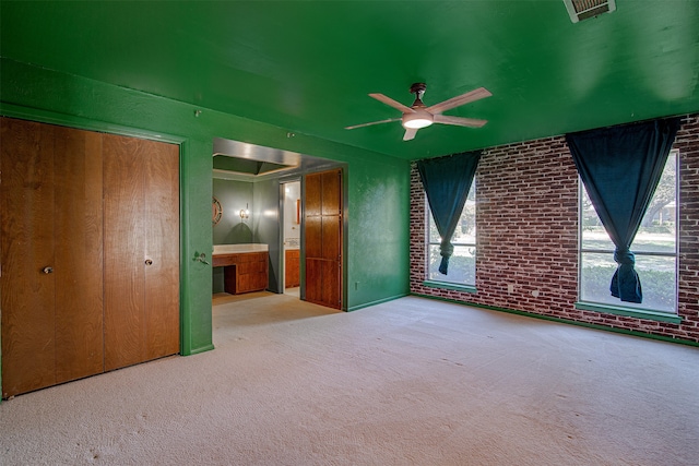 unfurnished bedroom with a closet, light colored carpet, ceiling fan, and brick wall