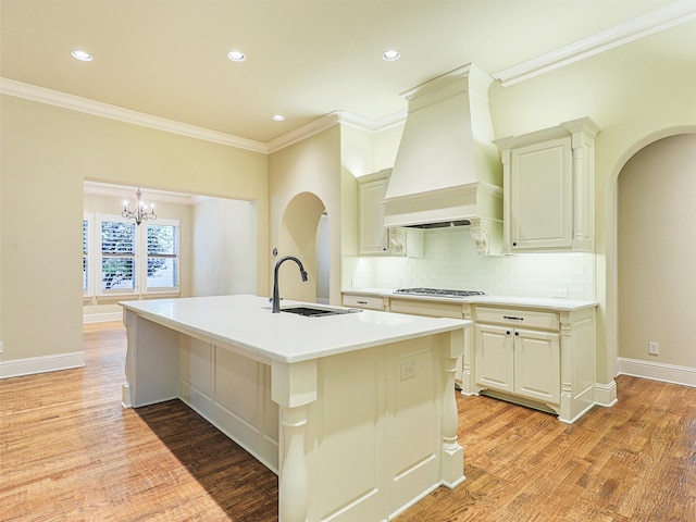 kitchen with a kitchen island with sink, light wood-type flooring, sink, ornamental molding, and premium range hood