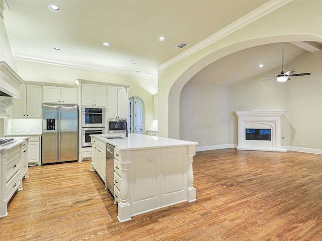 kitchen with an island with sink, lofted ceiling, light wood-type flooring, tasteful backsplash, and appliances with stainless steel finishes