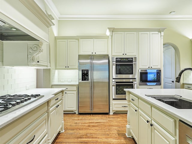 kitchen featuring light wood-type flooring, sink, backsplash, appliances with stainless steel finishes, and ornamental molding