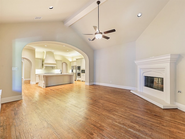 unfurnished living room with lofted ceiling with beams, ceiling fan, sink, light hardwood / wood-style flooring, and ornamental molding