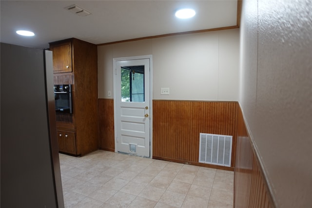 kitchen with black oven, stainless steel refrigerator, ornamental molding, and wood walls