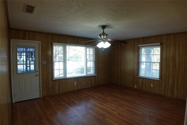 unfurnished dining area featuring wood walls, ceiling fan, dark hardwood / wood-style floors, and a textured ceiling