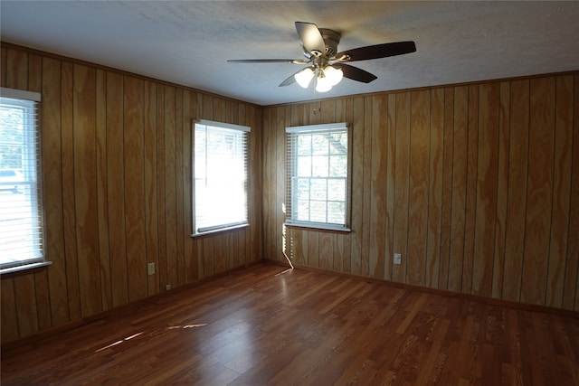 unfurnished room with a textured ceiling, wooden walls, dark hardwood / wood-style floors, and ceiling fan