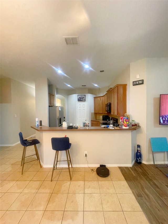 kitchen featuring black appliances, kitchen peninsula, light hardwood / wood-style flooring, and a breakfast bar