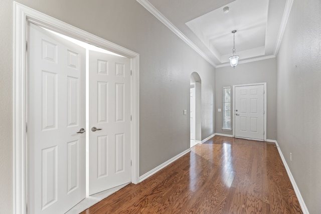 foyer entrance with ornamental molding, arched walkways, a tray ceiling, and wood finished floors