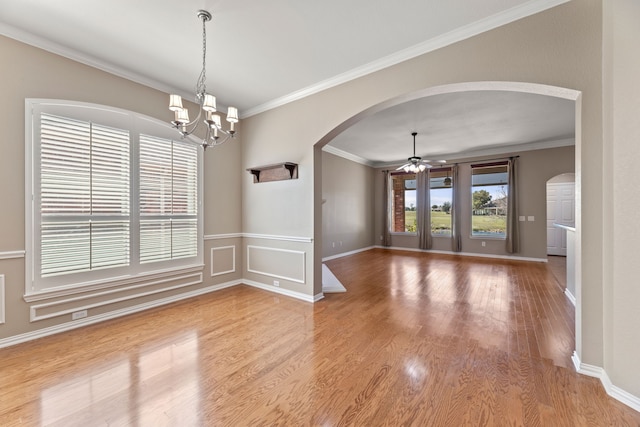 empty room featuring arched walkways, crown molding, wood finished floors, baseboards, and ceiling fan with notable chandelier