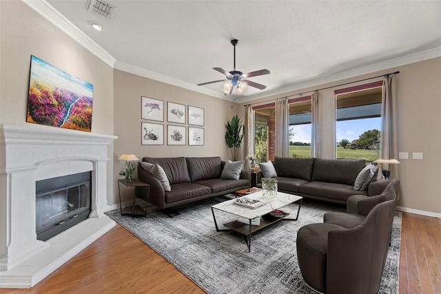 living room with light wood-style floors, a glass covered fireplace, visible vents, and ornamental molding