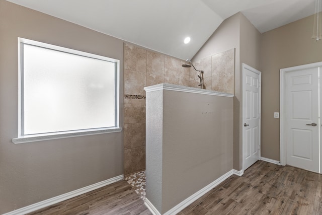 bathroom featuring lofted ceiling, wood finished floors, baseboards, and a walk in shower