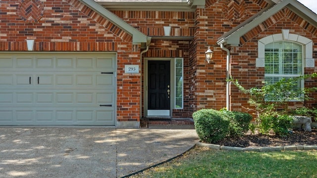 doorway to property featuring a garage, concrete driveway, and brick siding