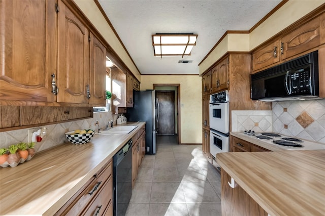 kitchen featuring black appliances, light tile patterned flooring, backsplash, and sink