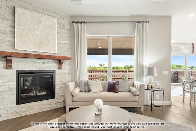 living room featuring wood-type flooring, a stone fireplace, and plenty of natural light