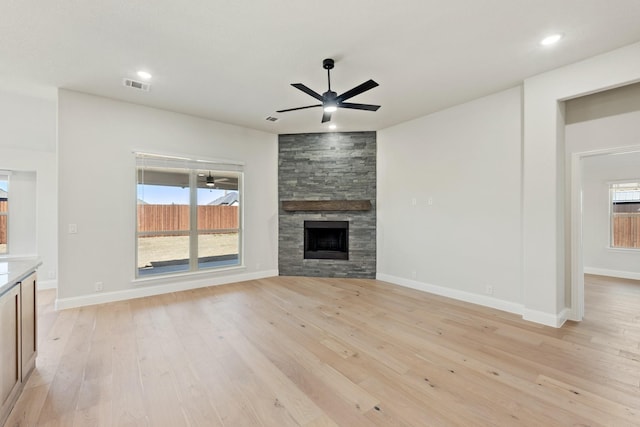 unfurnished living room with light wood finished floors, visible vents, a ceiling fan, a stone fireplace, and baseboards