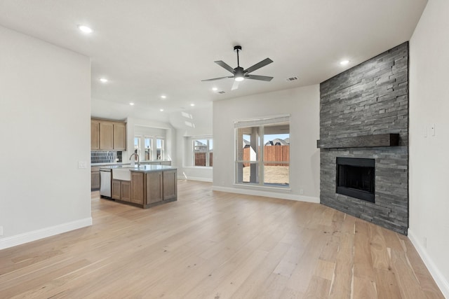 unfurnished living room with baseboards, a stone fireplace, a ceiling fan, and light wood-style floors