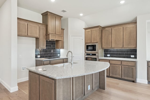 kitchen with tasteful backsplash, visible vents, a kitchen island with sink, black appliances, and a sink