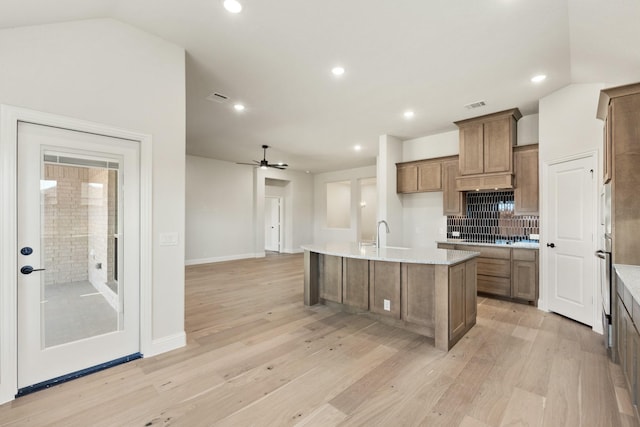 kitchen with lofted ceiling, visible vents, light wood-style flooring, brown cabinetry, and a kitchen island with sink