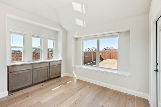 empty room with light wood-style flooring, baseboards, and vaulted ceiling