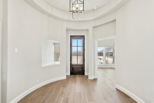 foyer entrance with a tray ceiling, baseboards, light wood finished floors, and an inviting chandelier