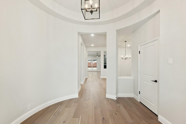 hallway featuring light wood-type flooring, a notable chandelier, and baseboards