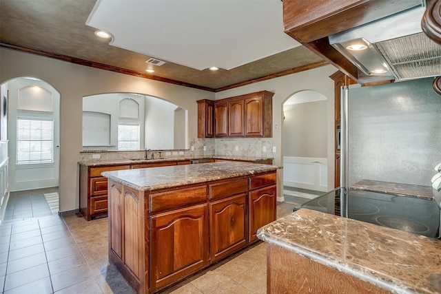 kitchen with light stone counters, sink, a kitchen island, stainless steel refrigerator, and crown molding