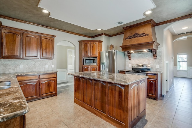 kitchen featuring stainless steel appliances, stone counters, a center island, custom exhaust hood, and ornamental molding