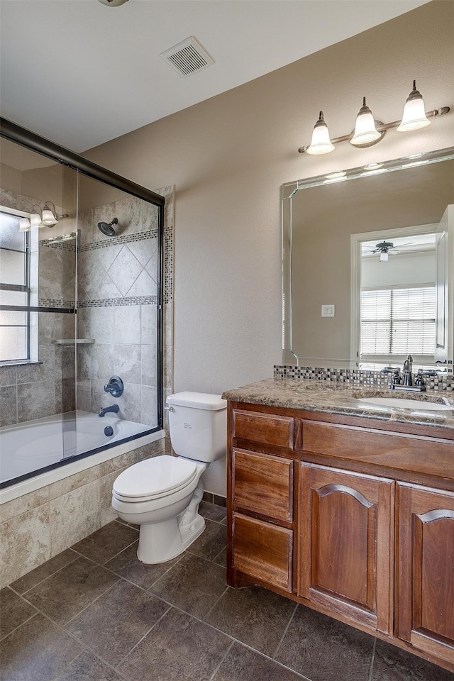 full bathroom with vanity, combined bath / shower with glass door, tile patterned flooring, ceiling fan, and toilet